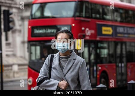 Pedestrian asian woman walks along Oxford Street wearing a face mask during the early stages of the coronavirus Covid 19 pandemic, London, UK Stock Photo