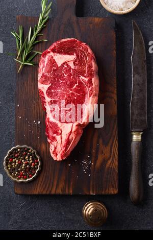 Top view Black Angus prime beef rib eye steak on cutting board with rosemary and spices on concrete dark background copy space Stock Photo