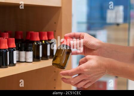 The hands of a female pharacist arranging normed brown glass apothecary bottles with sealed caps and droppers on a shelf Stock Photo