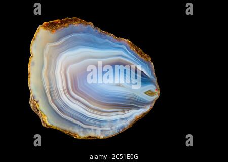 Close-up of polished agate gemstone with smooth icy surface texture  isolated on black background. Wavy pattern of concentric curves in cross section. Stock Photo