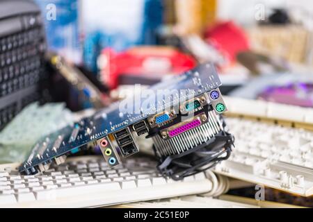 Spare video card on pile of computer keyboards. Colored hardware parts. Mainboard with circuit board, connector sockets and cooler. Electronic waste. Stock Photo