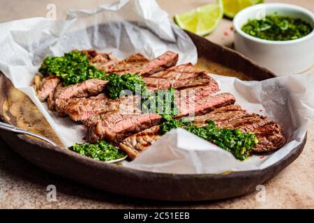 Sliced grilled beef steak with chimichurri sauce on a dark dish, dark background. Stock Photo