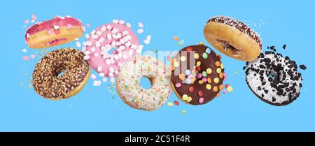 flying glazed round doughnuts. Mix of multicolored sweet donuts with sprinkles on blue background Stock Photo
