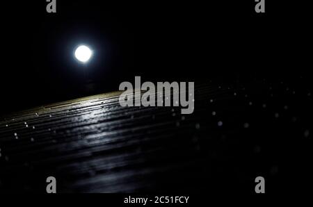 Looking up at a single small light illuminating part of a yellow-painted brick wall at night Stock Photo