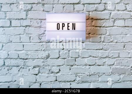 Open sign hanging on wall. Signboard OPEN of lightbox on white vintage brick wall background. Opening sign of cafe, bar, or restaurant. Business open Stock Photo