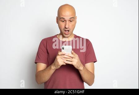 Shocked bald man is reading unbelievable news on his smartphone. Isolated on grey Stock Photo