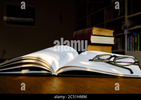 Close up of open text book with eye glasses on wooden desk in library. Old books and bookshelf background. Education concept. Selective focus Stock Photo