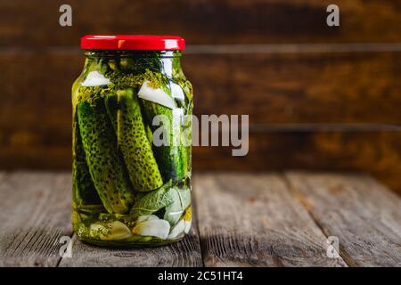 Pickled cucumbers in a jar on a wooden background, harvesting seasonal vegetables Stock Photo