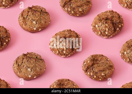 Brown bread buns with seeds on pink background, creative colorful pattern with small round dark bread Stock Photo