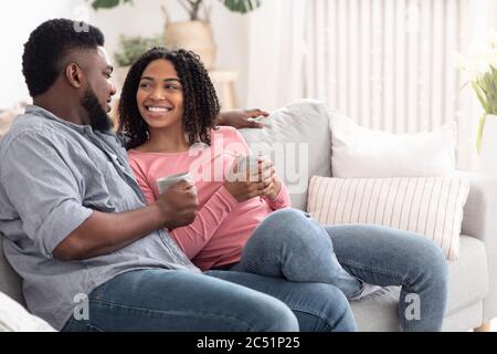 Black couple in love sitting on couch, drinking coffee and chatting Stock Photo