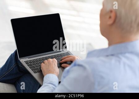 Elderly woman using laptop with black screen at home, mockup Stock Photo