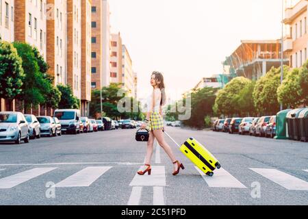 Young woman across the street with a yellow suitcase Stock Photo