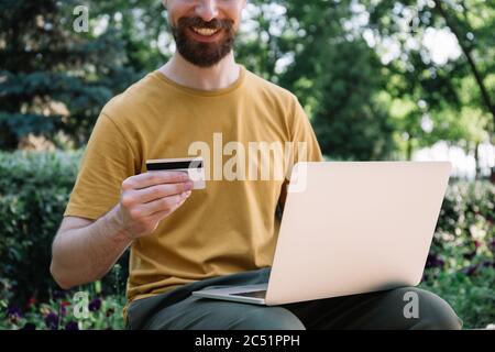 Man holding credit card, using laptop computer, online shopping. Successful freelancer receive payment Stock Photo