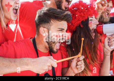 Red sport fans screaming while supporting their team out of the stadium - Football supporters having fun at competion event - Champions and winning co