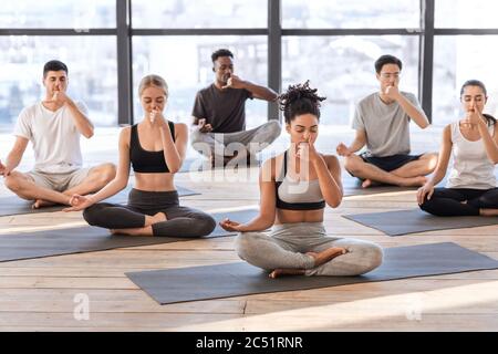 Young men and women in yoga studio practicing alternate nostril breathing exercises Stock Photo