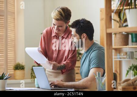 Portrait of smiling female assistant showing documents to handsome bearded man working at desk in modern office interior Stock Photo