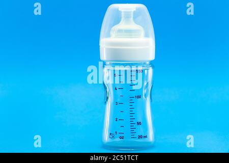 glass bottle with a measuring scale and a silicone pacifier for feeding babies, a transparent plastic cap isolated on a blue background with copy spac Stock Photo