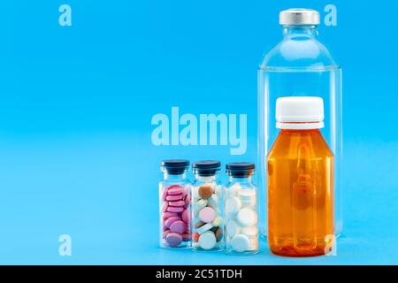 glass bottles with a vaccine for the treatment of viruses and bottles full of different pills, concept on a medical theme on a blue background with co Stock Photo