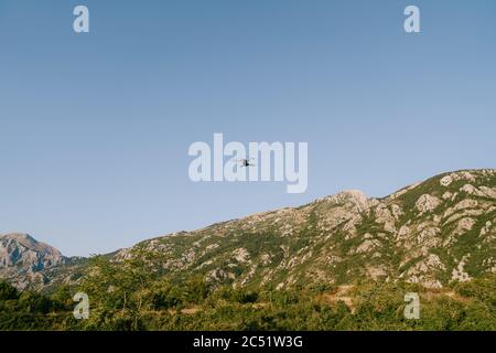 A small black drone flies over the green mountains.  Stock Photo