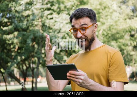 Emotional man using digital tablet, shopping online, watching movie. Excited guy looking at screen, celebration success, sport betting concept Stock Photo