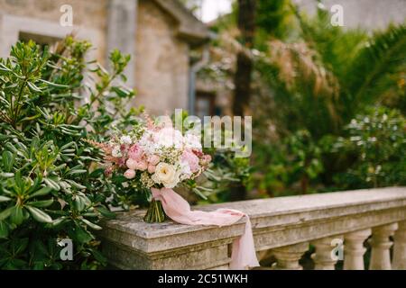 bridal bouquet of white and pink roses, peonies, delphinium, astilbe and white ribbons on the railing of an ancient staircase Stock Photo