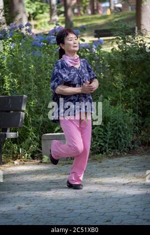 An Asian American woman dances vigorously to Chinese music for about 30 minutes. In Kissena Park, Flushing, New York City. Stock Photo