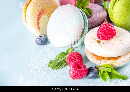 Colorful french macaron dessert. Set of various different tastes and color macaron cookies with berries, sugar powder and mint on blue background Stock Photo