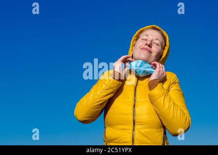 Close up portrait of a satisfied girl taking off his medical mask and inhaling fresh clean air on an open-air street during a coronovirus quarantine p Stock Photo