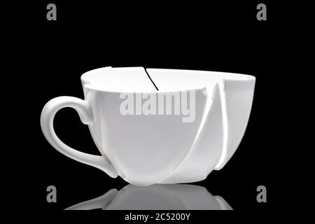 white ceramic cup broken into fragments as a result of the fall with reflection, a concept of a kitchen object on the theme of crisis on a black backg Stock Photo