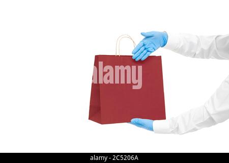 hands in blue sterile gloves of faceless courier for safe delivery of food in eco friendly red package shows palm at packet during quarantine of socia Stock Photo