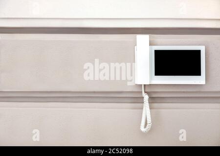 internal intercom with a handset for conversation and a video surveillance screen in a white body is suspended on the wall, closeup of a home security Stock Photo