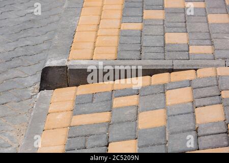Ramp for the descent of wheeled vehicles from the pedestrian sidewalk onto the road paved with stone tiles with a barrier border, closeup side view no Stock Photo