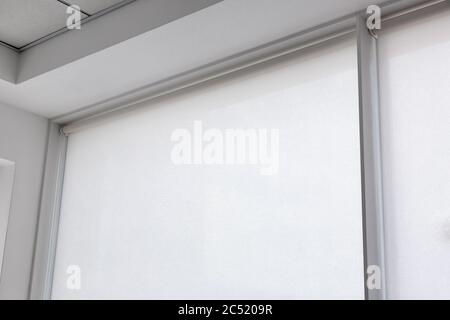 white rolled fabric blinds on the window in a room, indoor roll object of screen protection against sunlight close up with copy space. Stock Photo