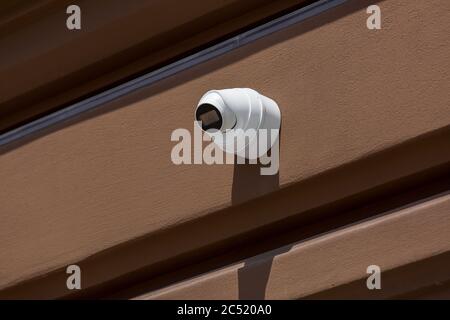 white CCTV camera installed on the exterior facade a brown building wall, close up video surveillance and crime tracking system. Stock Photo