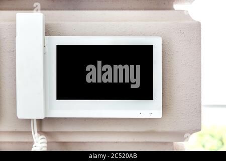 internal intercom with a handset for conversation and a video surveillance screen in a white case is suspended on the wall, close-up of a home securit Stock Photo