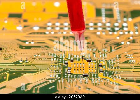 motherboard with contact paths of microcircuit and syringe with needle filled with red liquid, concept on topic of cospirology of vaccination and chip Stock Photo