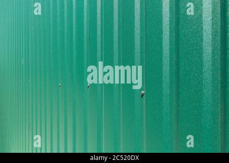 galvanized iron fence with corrugated vertical stripes closeup of texture of green roofing of sheet of green color side view, nobody. Stock Photo