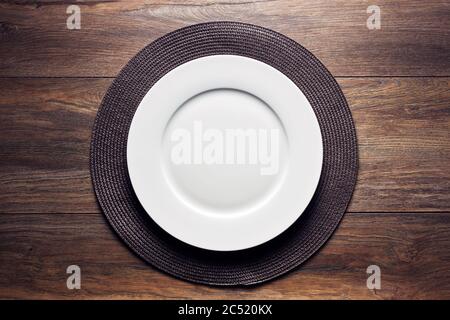 Empty white round plate with a serving mat on wooden table. Flatlay overhead view. Stock Photo