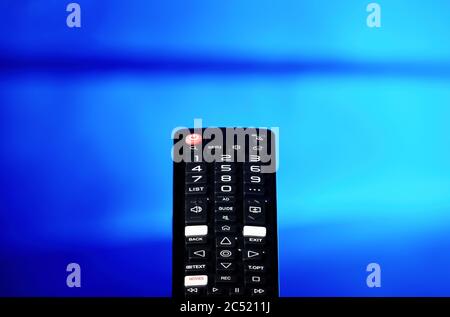 TV remote control pointing towards the television screen. Switching channels. Stock Photo