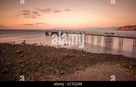 Llandudno pier at sunset on a calm evening. Warm sky at low tide exposing a rocky beach Stock Photo