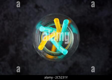 Yellow and blue plastic straws in an empty glass bottle on black background. Overhead or top view. Stock Photo