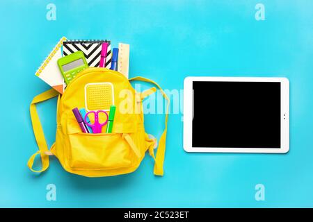 Back to school, education concept. Yellow backpack with school supplies Notebook, pens, ruler, calculator, scissors, tablet isolated on blue Stock Photo
