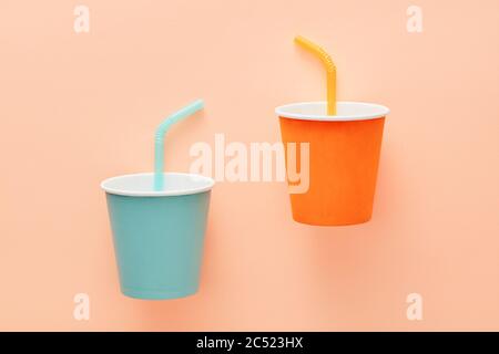 Blue and orange paper cups with straws on pale orange background. Flat lay overhead view Stock Photo