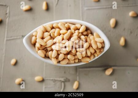 high angle view of a white ceramic bowl full of shelled pine nuts on a textured concrete surface Stock Photo