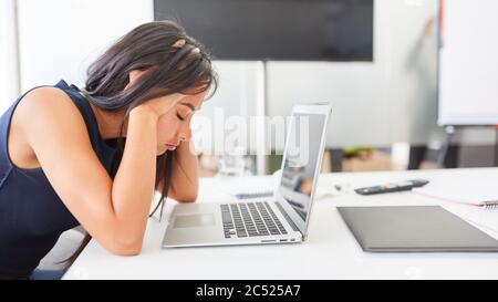 Young business woman sitting in office with headache on laptop computer because of overtime