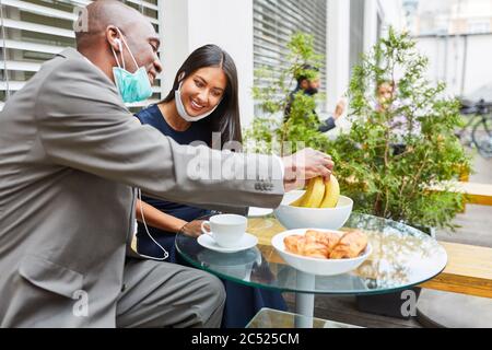 Business people in the lunch break in the cafe having small talk and snacking with mouth protection on the chin Stock Photo