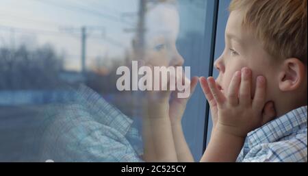 Close-up shot of a little boy traveling by train and looking out the window. His hands on the face and reflection in the glass Stock Photo