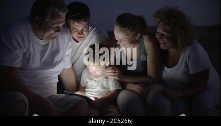 Parents and grandparents looking at boy using tablet computer. They sitting outdoor at night Stock Photo