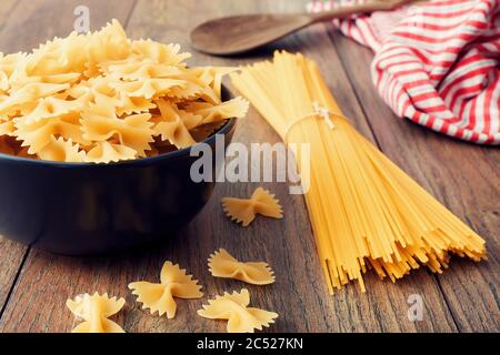 Spaghetti and farfalle or bow tie pasta in a bowl on wooden kitchen table. Close up view. Stock Photo