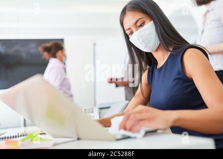 Businesswoman using face mask while disinfecting keyboard in office because of Covid-19 and corona virus Stock Photo
